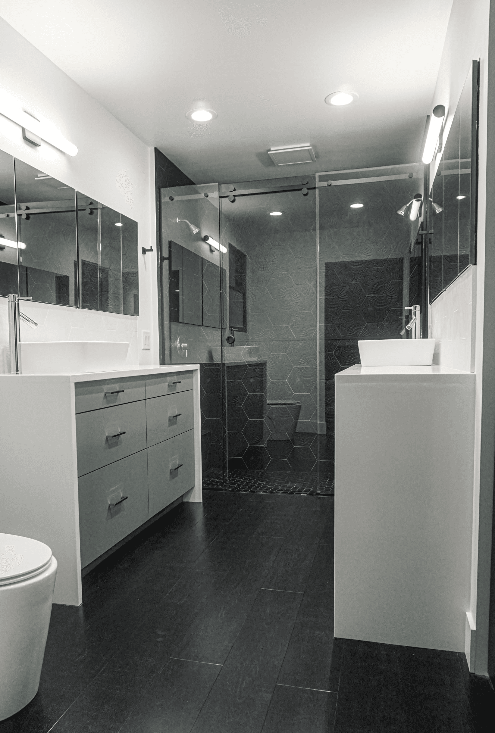 Completed primary bathroom with floating vanities and glass shower enclosure